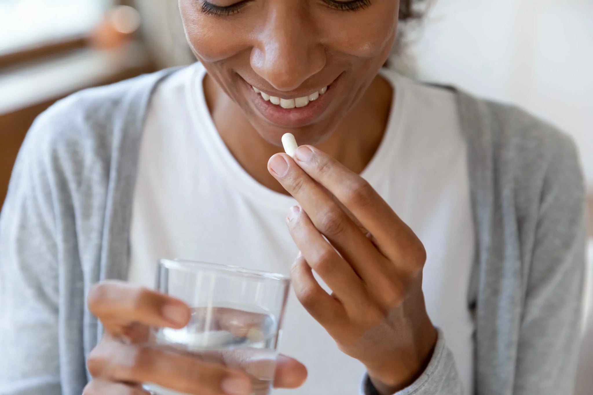 A person is holding a pill in one hand and a glass of water in the other.
