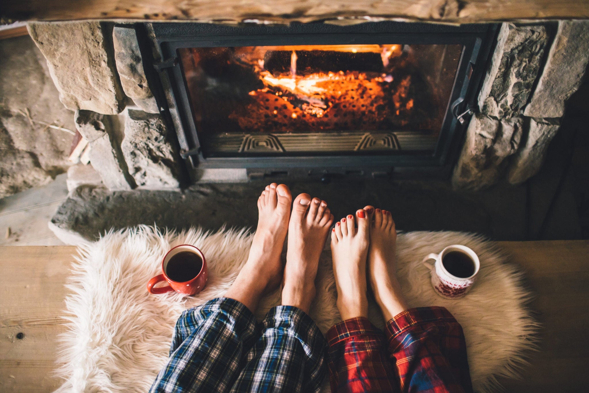 Two people are sitting with their legs outstretched, showing their feet in front of a cozy fireplace.