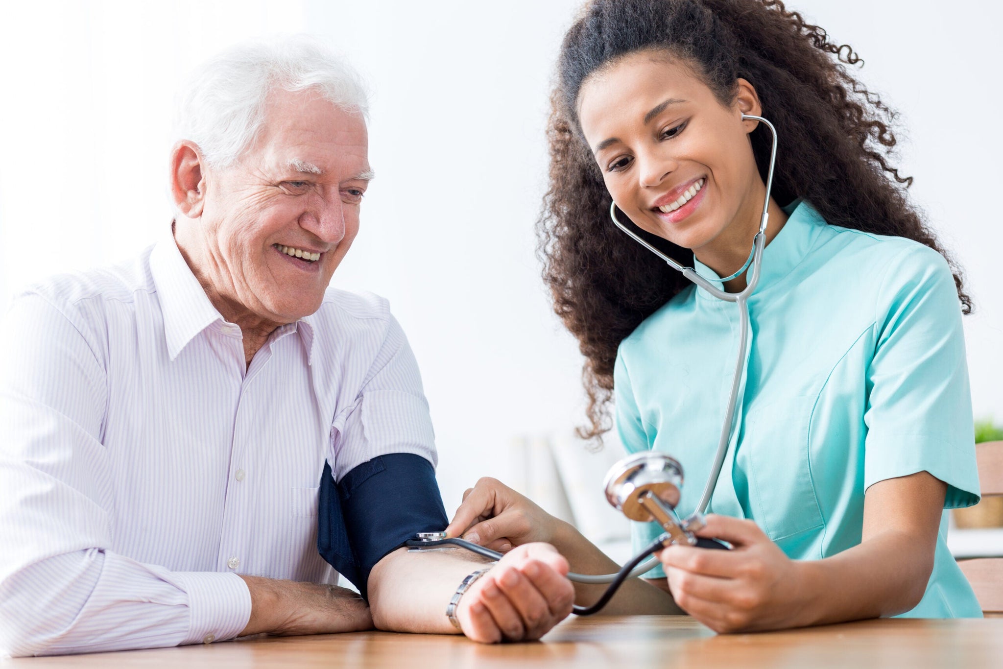 A smiling elderly man is getting his blood pressure checked by a healthcare professional.