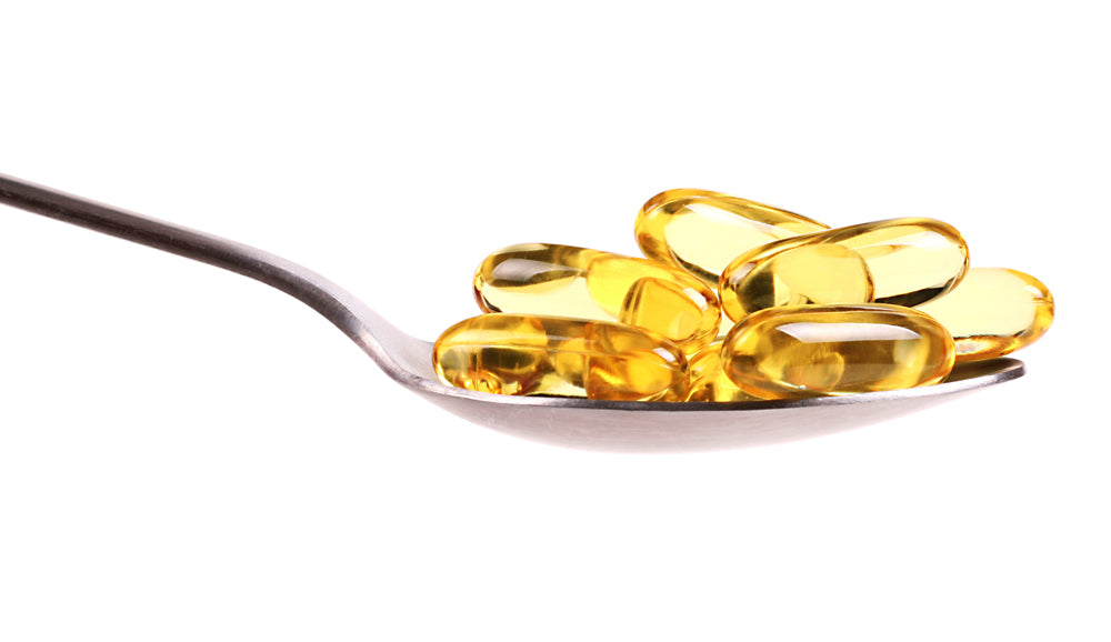 A metal spoon holds several glossy, yellow gel capsules filled with liquid against a plain white background.