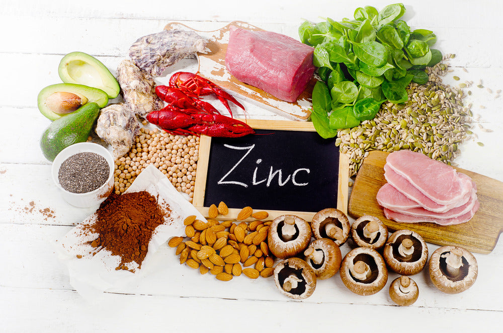 An assortment of zinc-rich foods displayed on a white wooden surface.