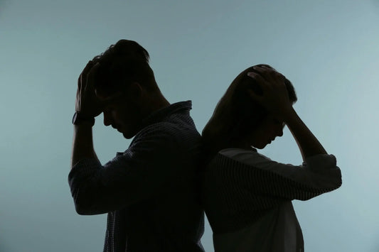 Silhouetted image of a man and a woman standing back to back, both holding their heads in their hands as if experiencing stress or frustration.