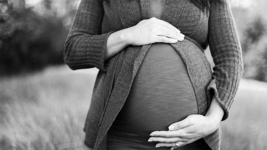 A black-and-white image showing a pregnant woman cradling her large belly with both hands.