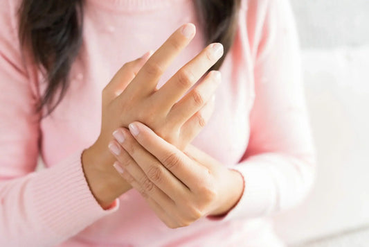 Close-up of a person wearing a pink long-sleeve top, holding their left hand with their right hand, appearing to massage the fingers.