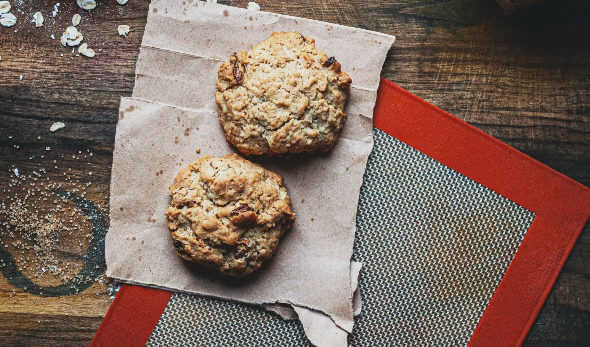 Two oatmeal cookies rest on a piece of brown parchment paper.