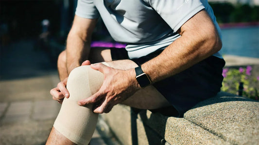 A person wearing a light blue shirt and black shorts is sitting on a stone bench outdoors, their knee wrapped in a beige compression bandage.
