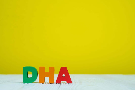 Colorful wooden letters spelling "DHA" are arranged on a light wooden surface against a vibrant yellow background.