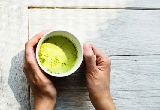 A pair of hands is holding a white cup filled with green tea, one of the finest anti-inflammatory drinks to treat arthritis.