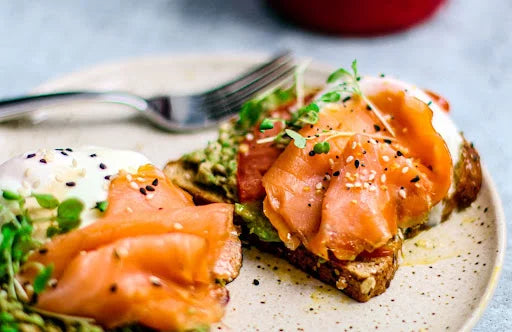 A close-up of a dish featuring two pieces of toast topped with sliced smoked salmon, avocado spread, poached eggs