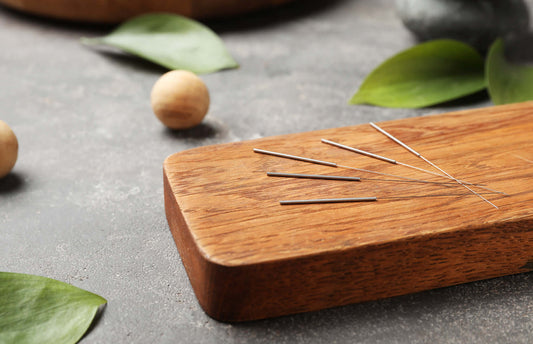 Thin acupuncture needles are neatly arranged on a rectangular wooden board.