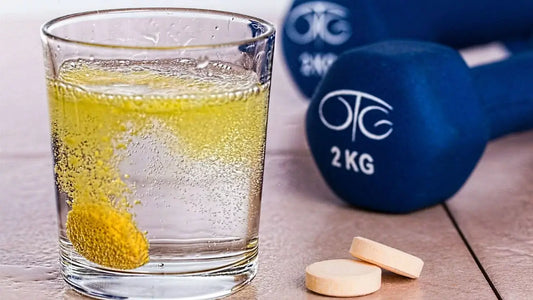 A dissolving yellow effervescent tablet fizzes in a glass of water next to two more tablets on a table