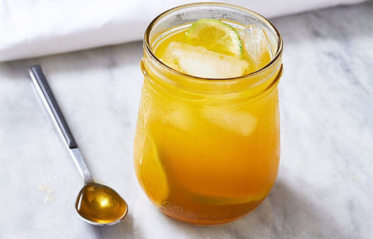 A rustic glass jar filled with a vibrant yellow-orange drink, garnished with lime slices and ice cubes