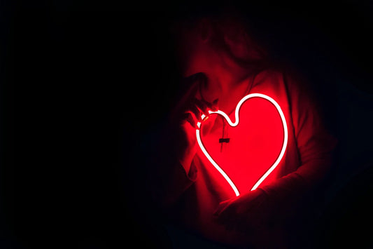 A person in low light holds a bright red neon heart, akin to asking, "Can omega-3 reduce heart attacks?"