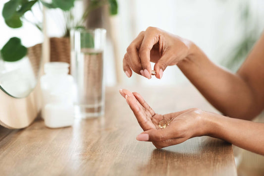 Close-up of a person holding several vitamin capsules in one hand and picking one up with the other hand, near a wooden table.