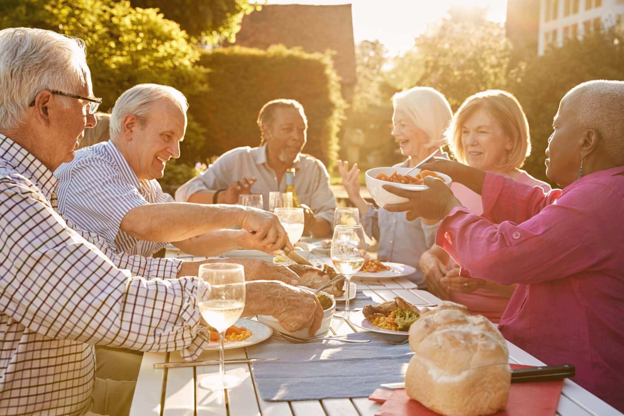 A group of older adults seated around an outdoor table, sharing a meal loaded with foods rich in Omega-3 fatty acids — an undercover love story for the liver.
