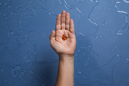 A hand is shown with its palm open against a blue background with water droplets.