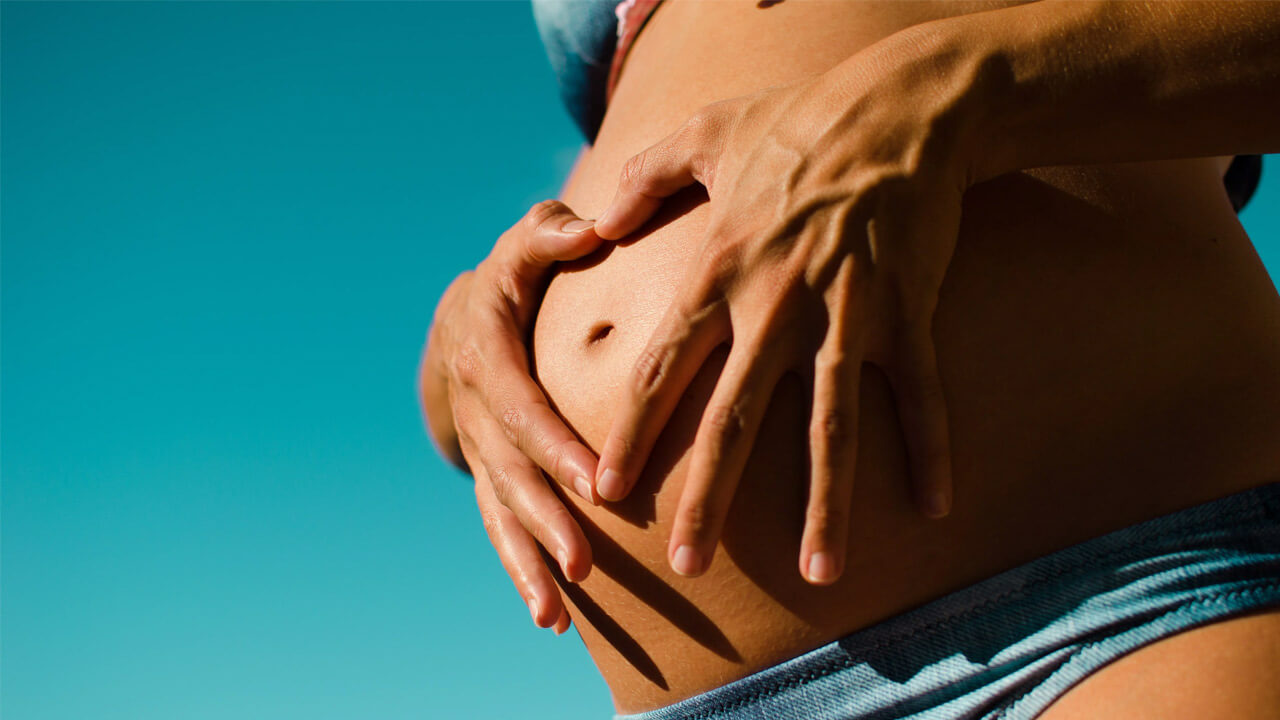 Close-up of a person’s bare pregnant belly, cradled by their hands.