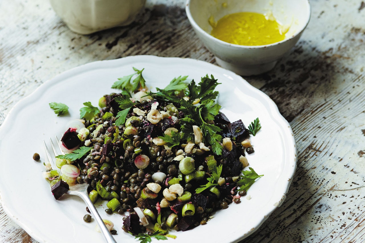A plate of mixed lentil salad with chopped vegetables, herbs, and nuts is displayed on a rustic wooden table.