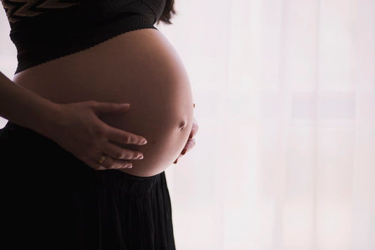 A pregnant woman gently cradles her belly with both hands. She is wearing a black skirt and a dark top.