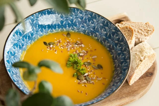 A blue patterned bowl filled with pumpkin soup garnished with seeds and a sprig of parsley.